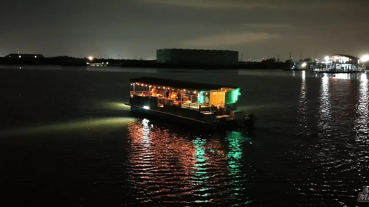 An illuminated passenger boat on the water at night, with lights reflected on the surface.