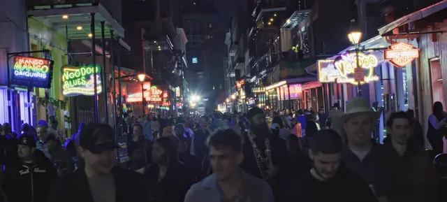 A crowd filling a neon-lit New Orleans street at night